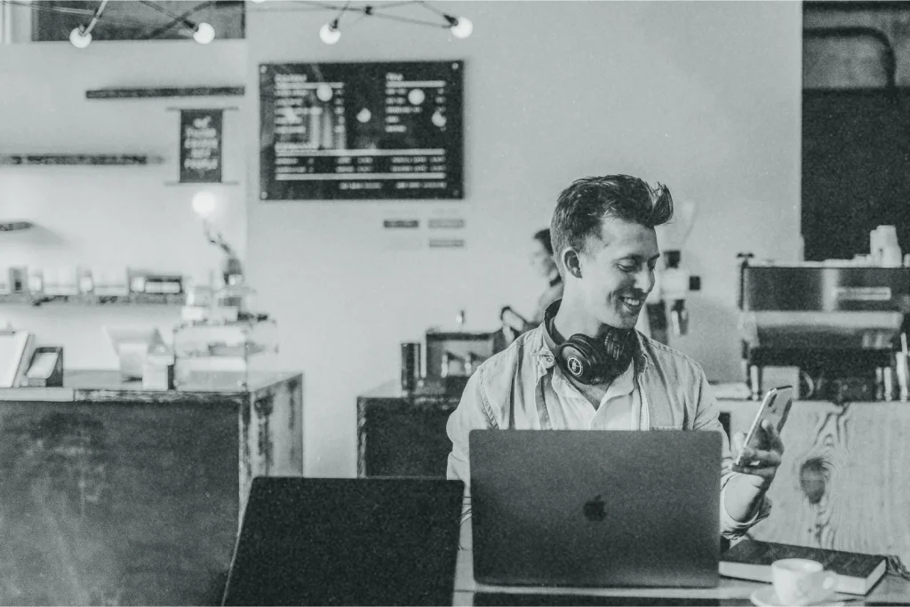 An image of a young man working on a laptop in a coffee shop.